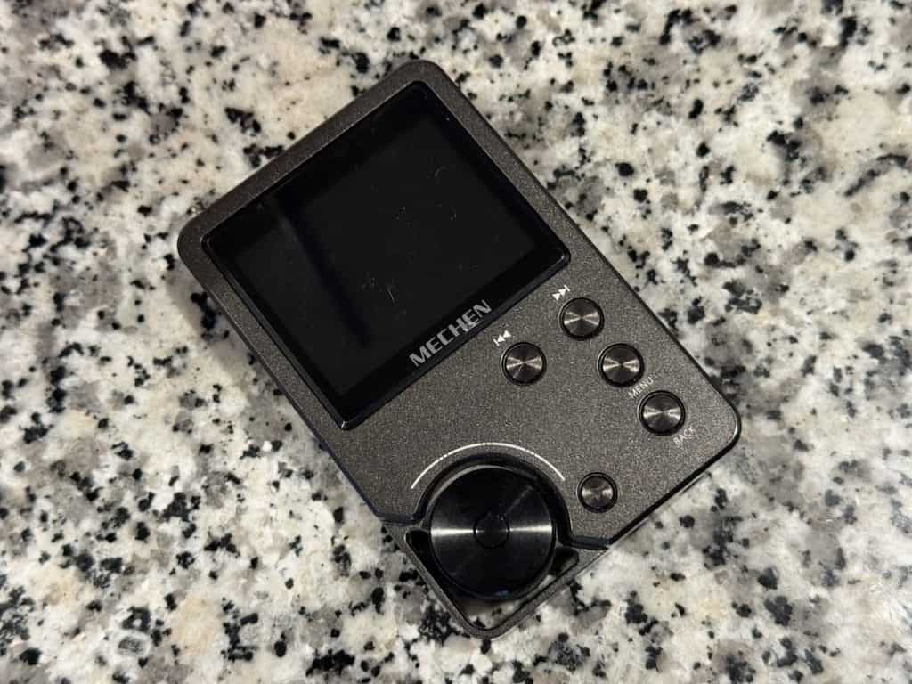 A music player. It's a rectangular metal block with a wheel on its lower left corner. The screen takes up almost the entire upper half of the block, and five hardware buttons arranged in a backward C are on the lower right side of the rectangle. The brand name -- printed on the bezel of the screen at its bottom -- is "MECHEN."
