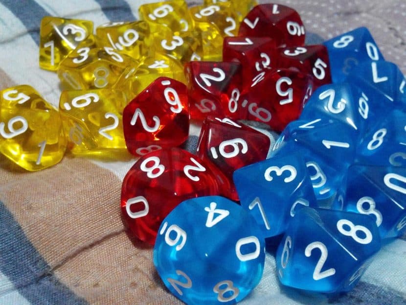 A close-up of rows of 10-sided dice in translucent plastic. From left to right the rows are yellow, red, and blue.
