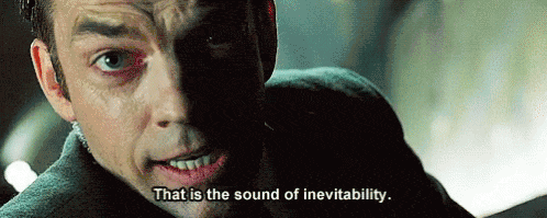 Agent Smith, the bad guy in a suit and an earpiece from The Matrix, holds a struggling Neo (just off-camera) as he stares down an oncoming train, saying, "That is the sound of inevitability."