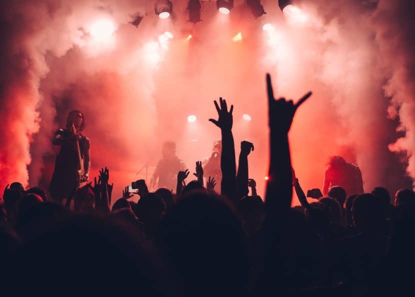 A stage lit by red lights shining through clouds of smoke is barely visible behind hands thrown into the air by the audience.