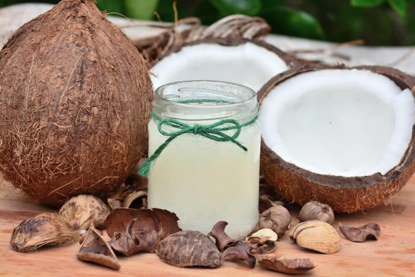 Two coconuts -- one split in halves and one whole -- flank a glass of coconut milk decorated with green yarn. Pieces of coconut husk litter the table in front of it.