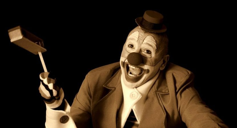 A sepia-toned image of a broadly grinning clown in a tiny bowler hat and a tweed suit twirling a noisemaker.
